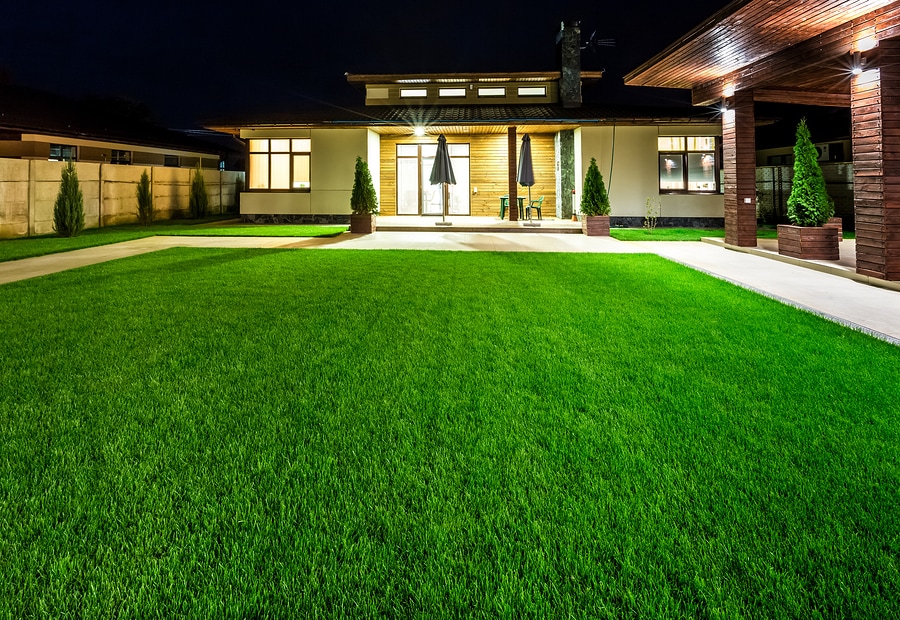 Nighttime shot of courtyard and front and side of house with beautifully manicured lawn